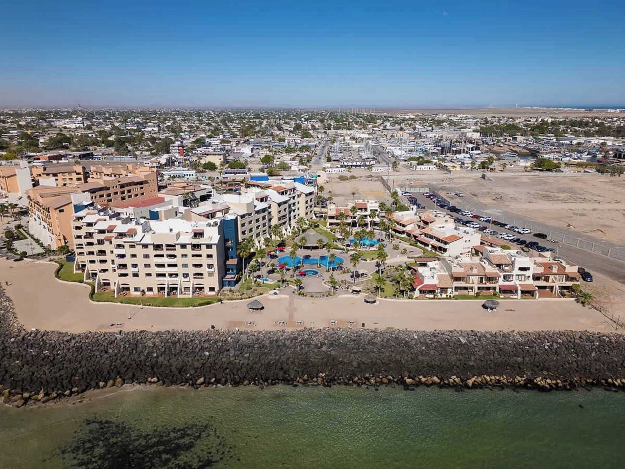 A coastal hotel with multiple buildings, a beach, and a rocky shoreline.