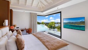 Ett modernt hotellrum med en stor säng, ett skrivbord och utsikt över ett tropiskt landskap genom en glasdörr.