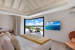 A bedroom with a large bed, a TV mounted on the wall, and a view of the sea through an open door. - Villa Sole Luce -- Prestige property near the beach (Les Terres Basses)