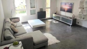 Een moderne woonkamer met een grote flatscreen televisie, een bank, een salontafel en een tv-meubel met planken.