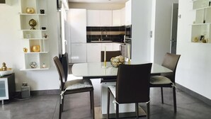 Een moderne keuken met witte kasten, een zwarte spatwand en een eethoek met een glazen tafel en stoelen.