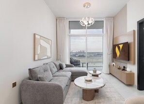 Ett modernt vardagsrum med en grå hörnsoffa, ett runt soffbord, en tv som är monterad på väggen och ett stort fönster med utsikt över stadsbilden.