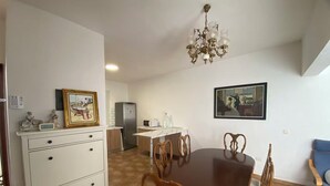 Un comedor con una mesa y sillas de madera, un armario blanco con cajones, un refrigerador y una araña.