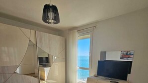 A modern hotel room with a bed, a TV, a large window with a view of the sea, and a mirror. - Experience a fantastic stay at Dolce Vita apartment, right next to the beach! (Durrës)