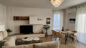 A modern living room with a sofa, coffee table, TV, and dining area. - Experience a fantastic stay at Dolce Vita apartment, right next to the beach! (Durrës)