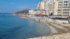 A coastal hotel with a beach view, a pier, and a mountain in the background. - Experience a fantastic stay at Dolce Vita apartment, right next to the beach! (Durrës)