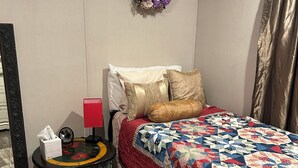 A bedroom with a wooden floor, a bed with a red and white quilt, a small round table with a fan and tissues, a mirror, and a decorative wreath on the wall. - Nature At the Cozy House (Slidell)