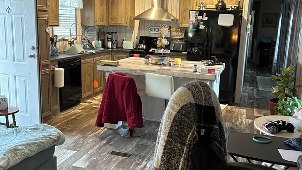A modern kitchen with wooden cabinets, a central island, and a dining area with a chair and table. - Nature At the Cozy House (Slidell)