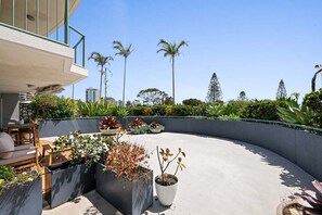 Una terraza en la azotea con un borde de hormigón curvo, muebles de exterior y varias plantas en macetas.
