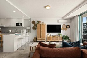 Una cocina moderna con armarios blancos, una isla central con taburetes y un televisor de pantalla plana, además de un área de comedor con mesa y sillas.
