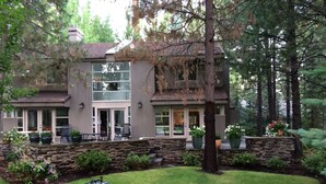 Une maison à deux étages avec des fondations en pierre, une terrasse dotée de mobilier d’extérieur et une pelouse bien entretenue.