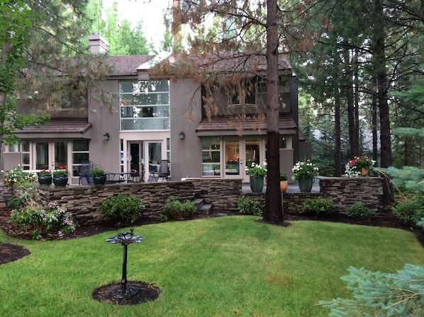 Una casa de dos pisos con base de piedra, un patio con mobiliario exterior y un césped bien cuidado.