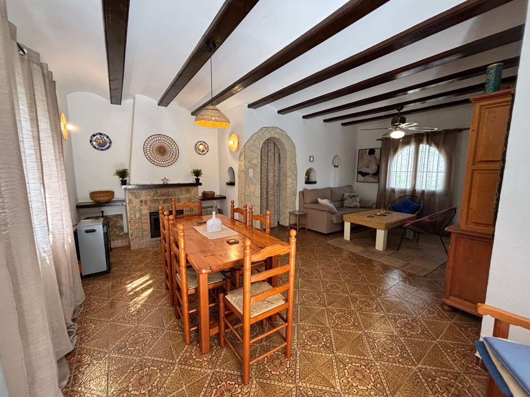 Un amplio espacio de sala con una mesa y sillas de madera, una chimenea de piedra y una zona de estar acogedora con un sofá y sillones.