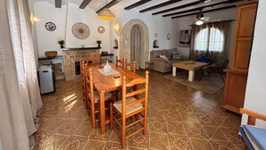 A spacious living area with a wooden dining table and chairs, a stone fireplace, and a cozy seating area with a sofa and armchairs. - Casa Estrella - Natural Mountain Retreat (Dénia)