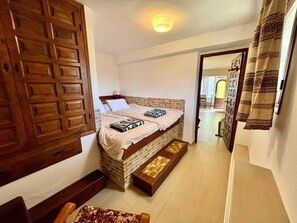 A bedroom with a bed, wooden wardrobe, and a small seating area.