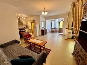 A living room with a sofa, a coffee table, and a dining area with chairs and a table. There is a kitchen area with a refrigerator and a microwave.