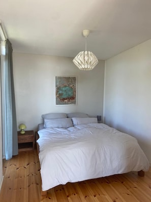 A bedroom with a bed, a nightstand, a lamp, a wall-mounted artwork, and a hanging light fixture.
