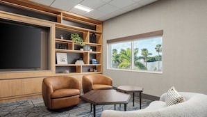 A modern room with a large flat-screen TV, two leather armchairs, a small table, a sofa, and a window with a view of palm trees. - Holiday Inn Express & Suites Miami Intl Airport - 36th St (Miami)