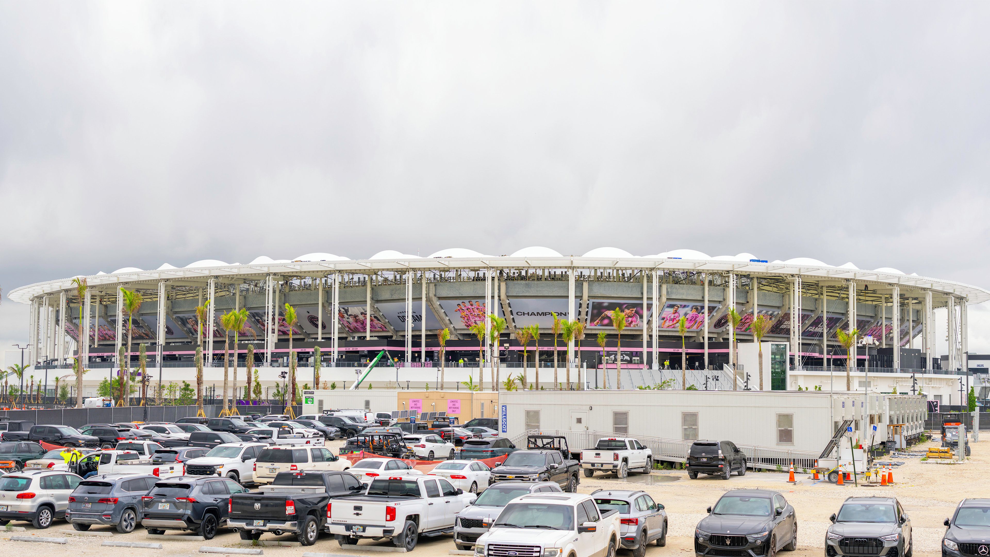 Un estadio grande con varios niveles de asientos y un estacionamiento lleno de vehículos.