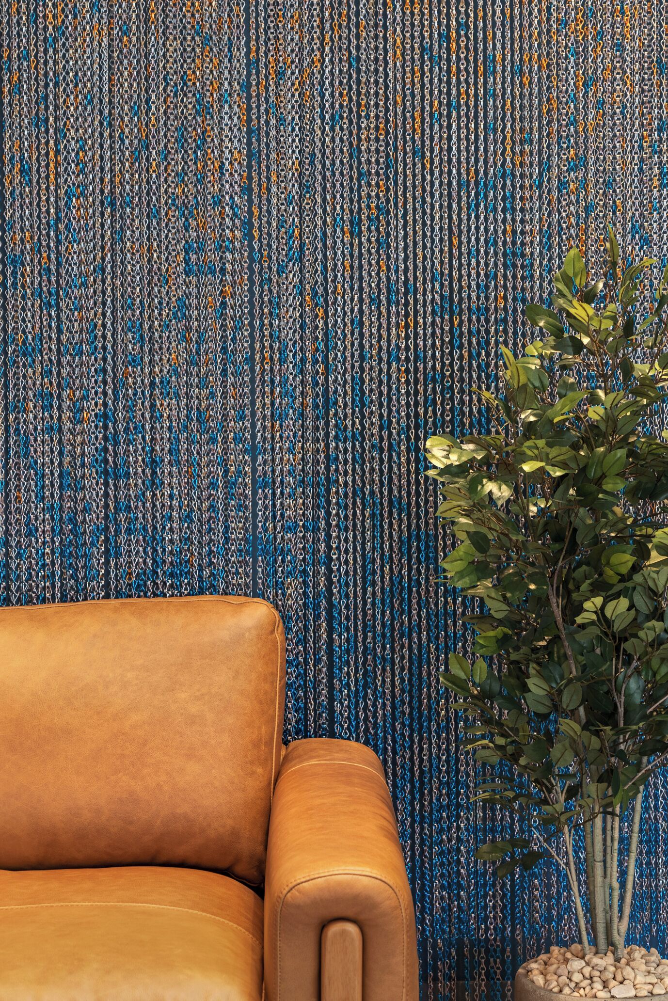 A leather armchair and a potted plant against a textured wall.