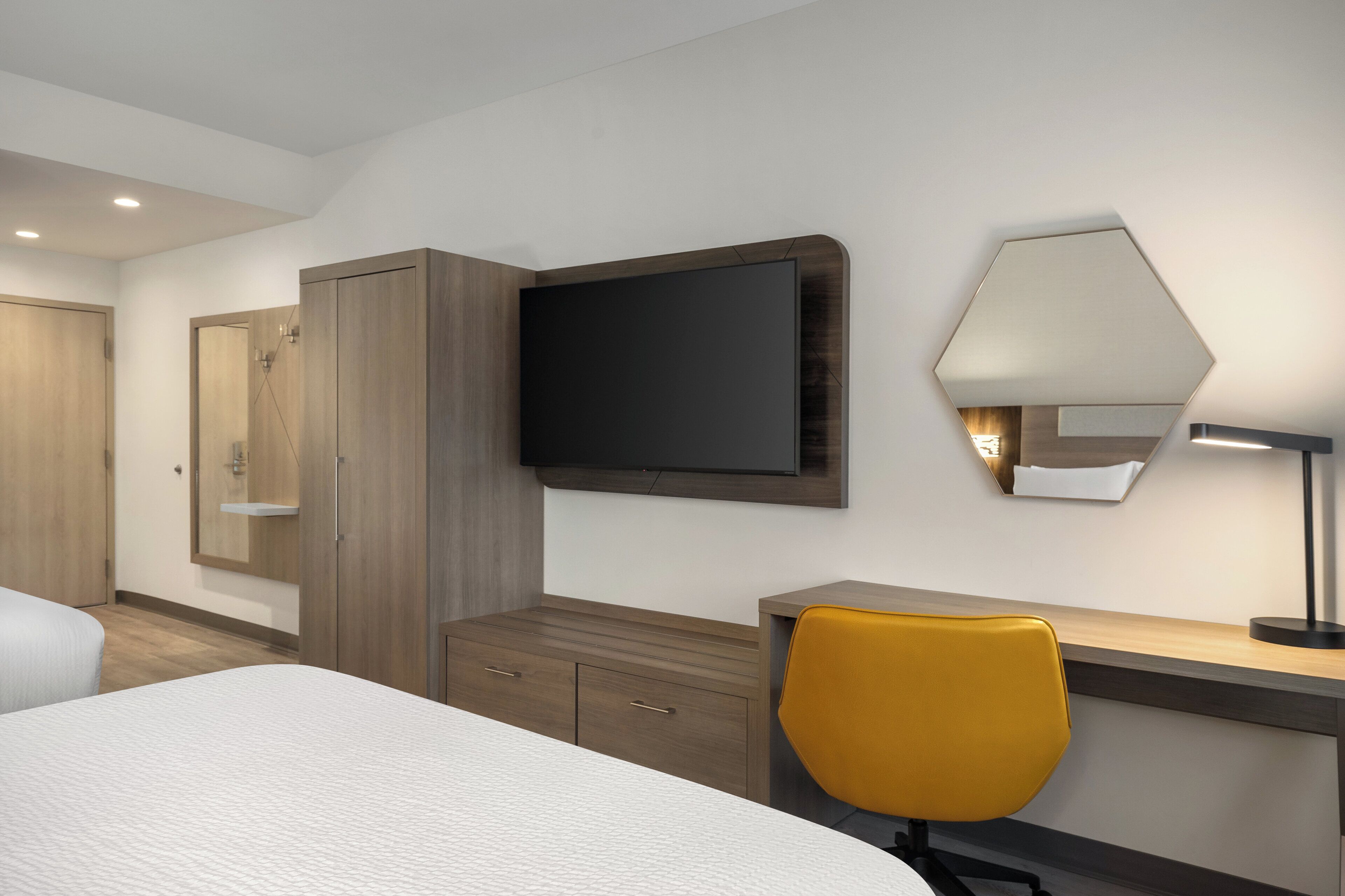 Habitación de hotel con cama, escritorio, silla, armario, televisión de pantalla plana y lámpara.