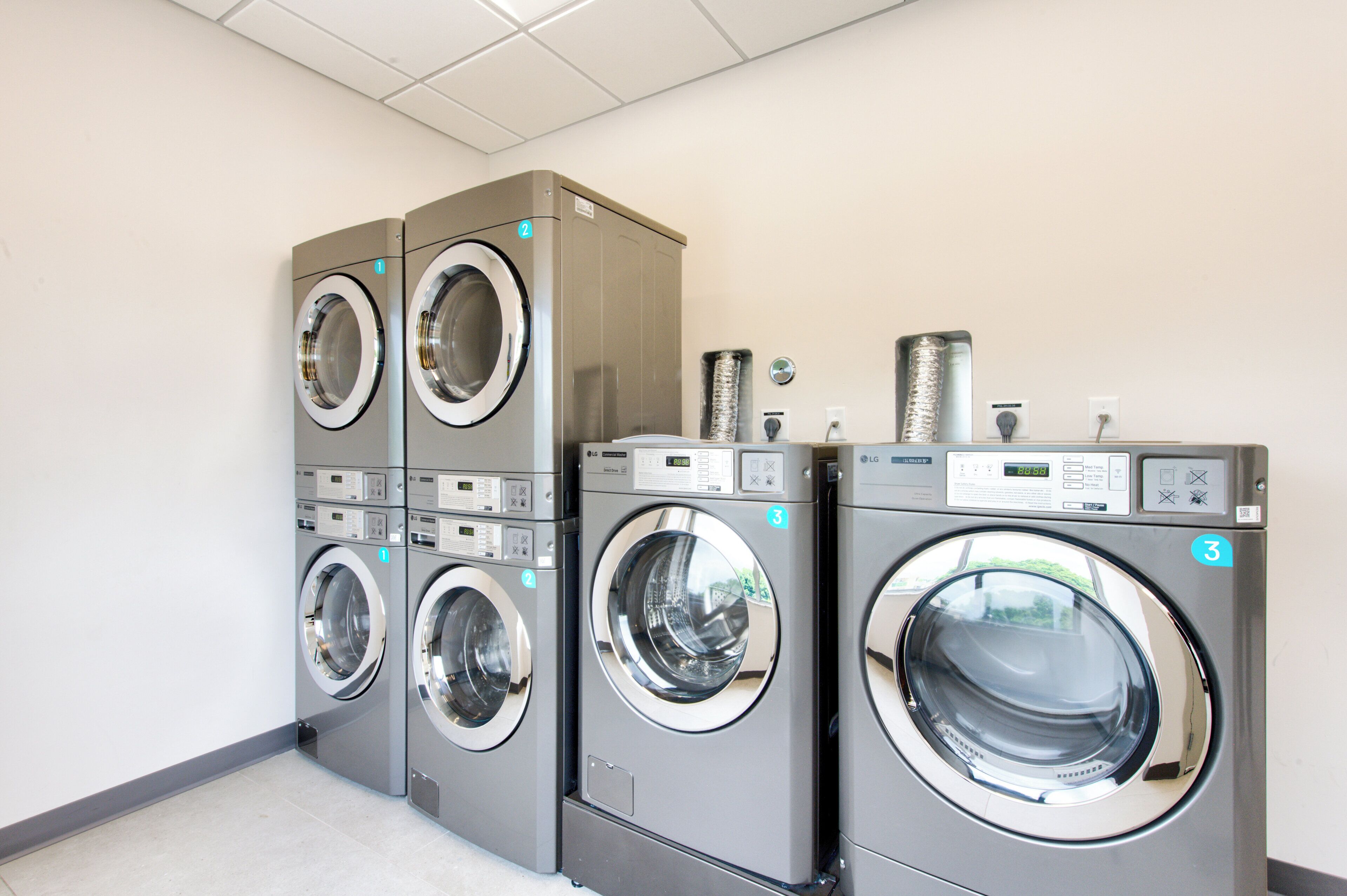A row of three stacked front-loading washing machines in a commercial laundry area.