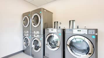 A row of three stacked front-loading washing machines in a commercial laundry area.