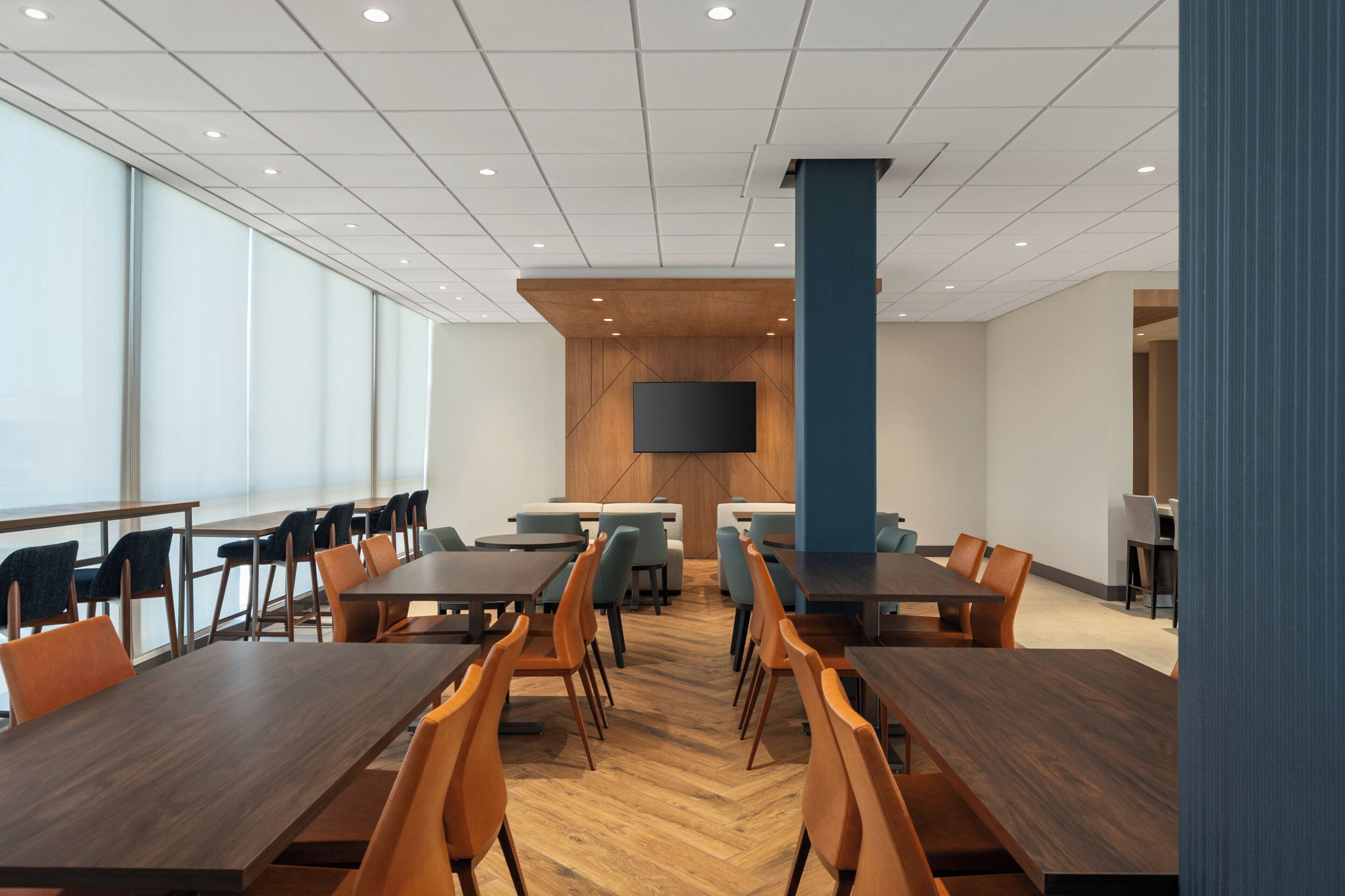 Une salle de conférence dotée de plusieurs tables et chaises, d’un grand téléviseur à écran plat fixé au mur et d’un mur décoratif en bois.