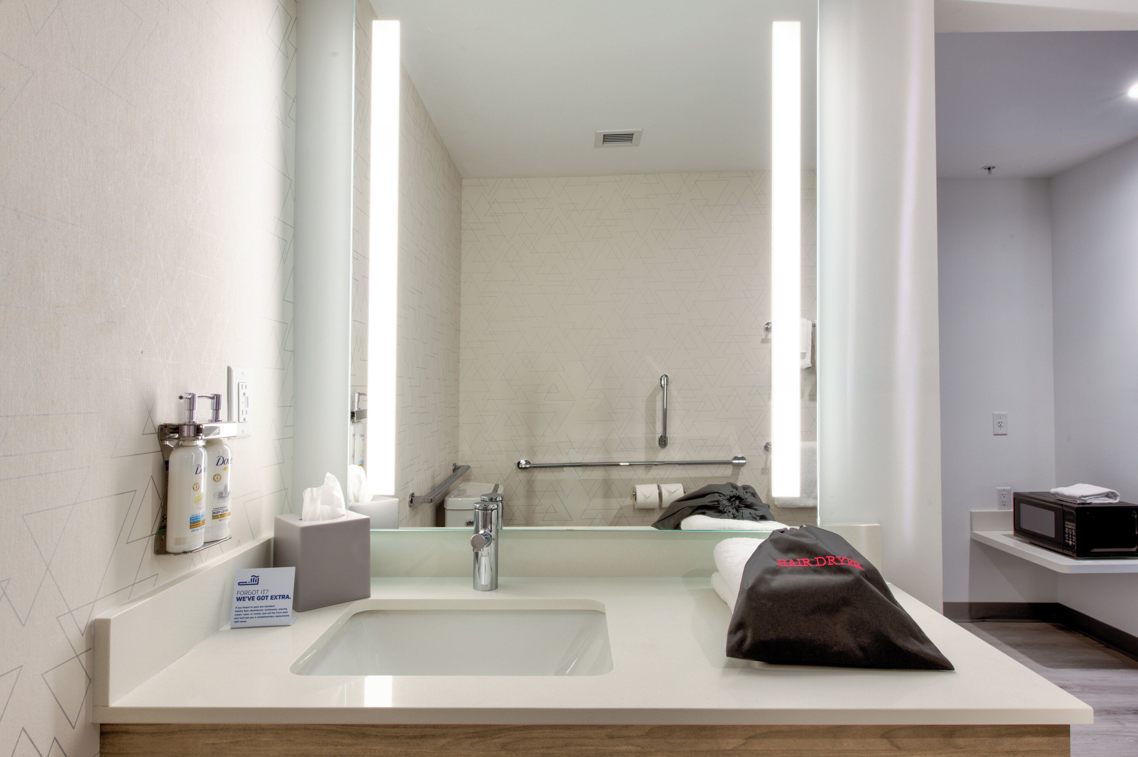 A hotel bathroom with a large mirror, a sink, a towel, a hairdryer, and toiletries.