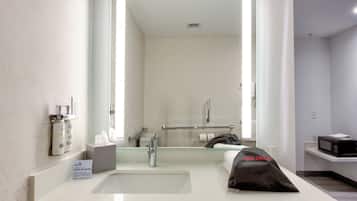 A hotel bathroom with a large mirror, a sink, a towel, a hairdryer, and toiletries.
