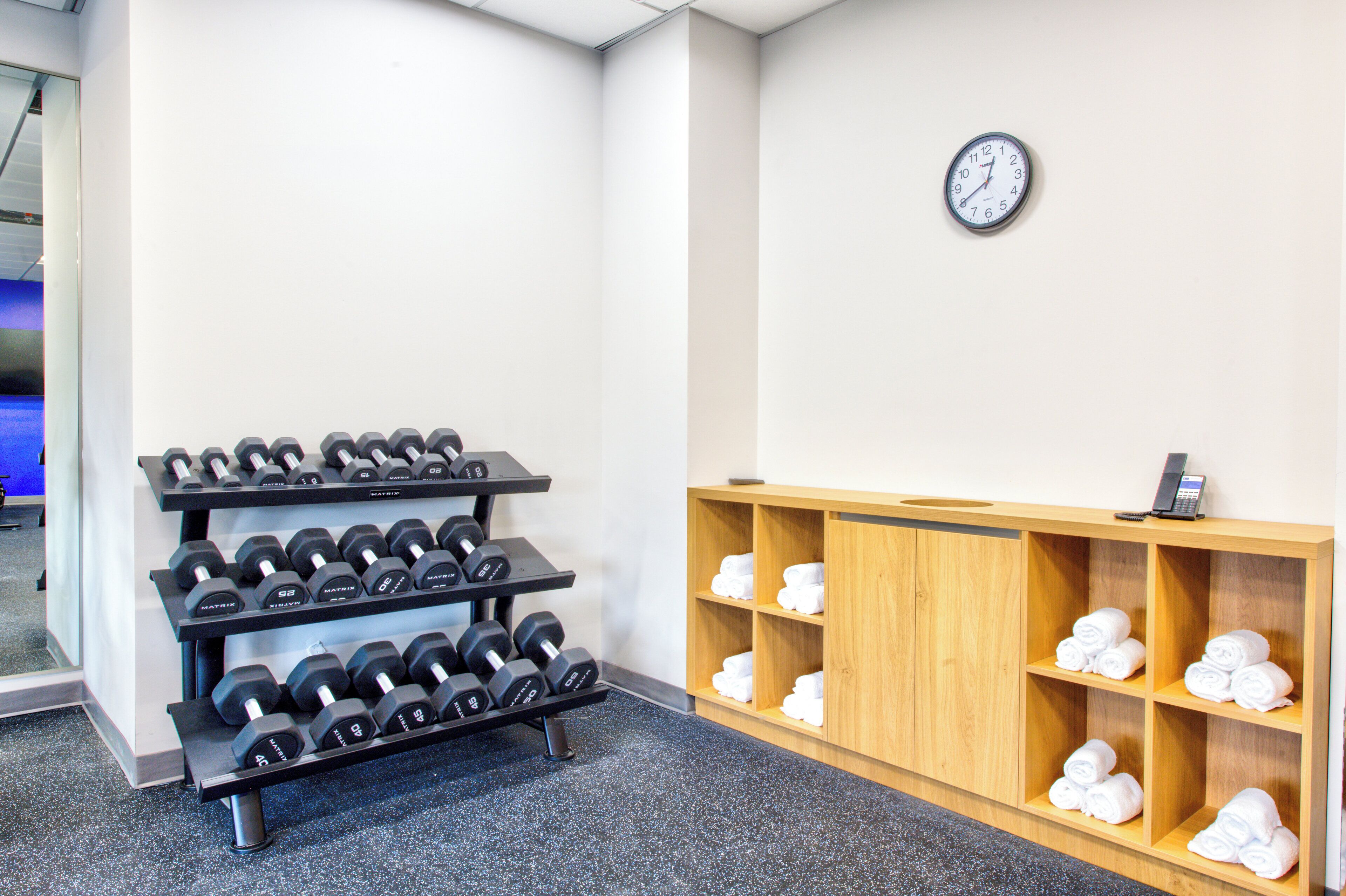 Zona de gimnasio con un estante de mancuernas y un estante de madera con toallas.