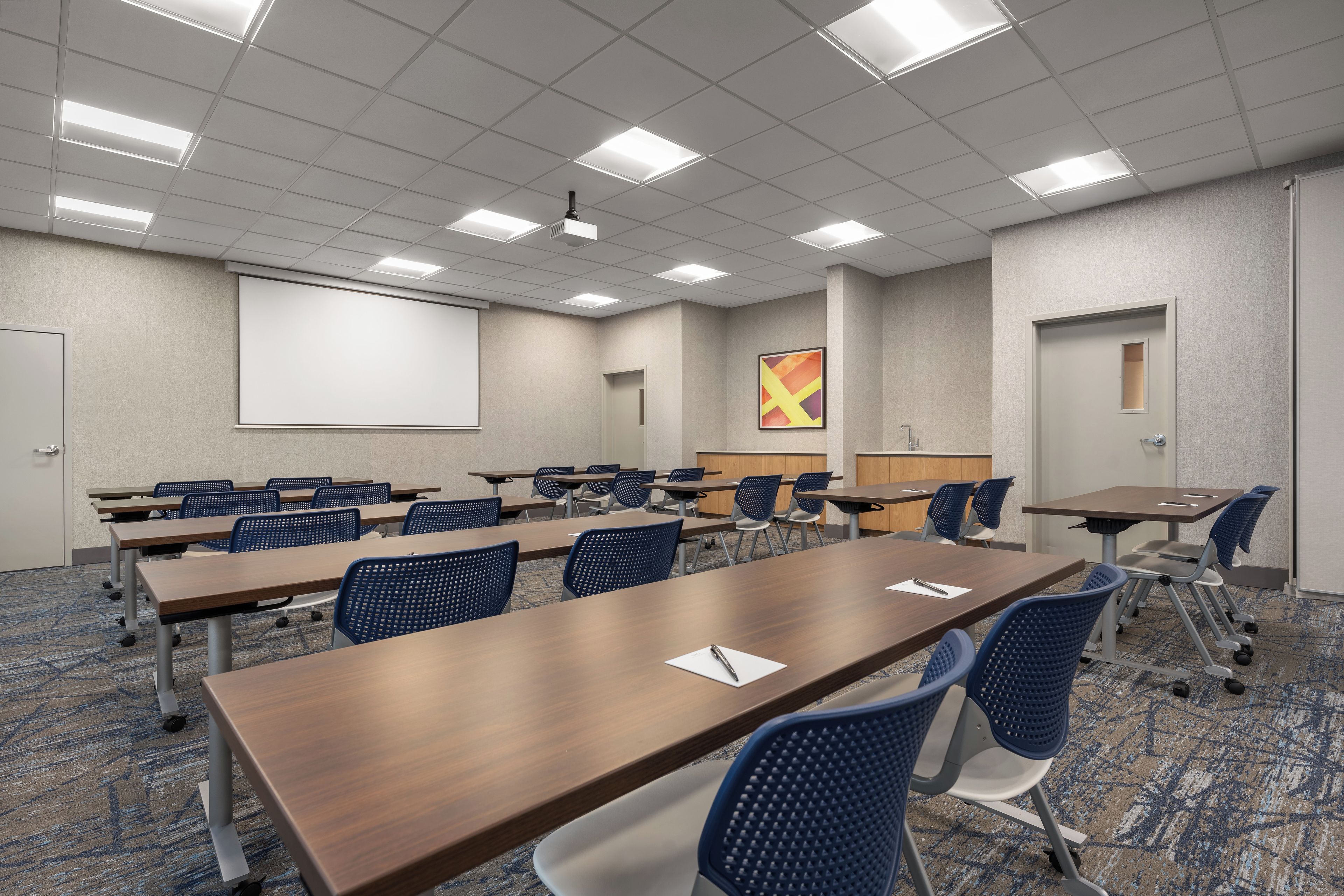 A conference room with a large screen, multiple tables, and chairs.