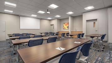 A conference room with a large screen, multiple tables, and chairs.
