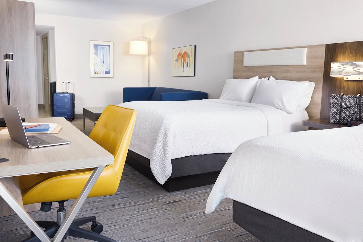 Ein Hotelzimmer mit zwei Betten, einem Schreibtisch mit einem Laptop, einem Stuhl und einem Koffer.
