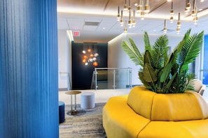 A modern lobby with a yellow sofa, a potted plant, and a glass elevator. - Holiday Inn Express & Suites Miami Intl Airport - 36th St (Miami)