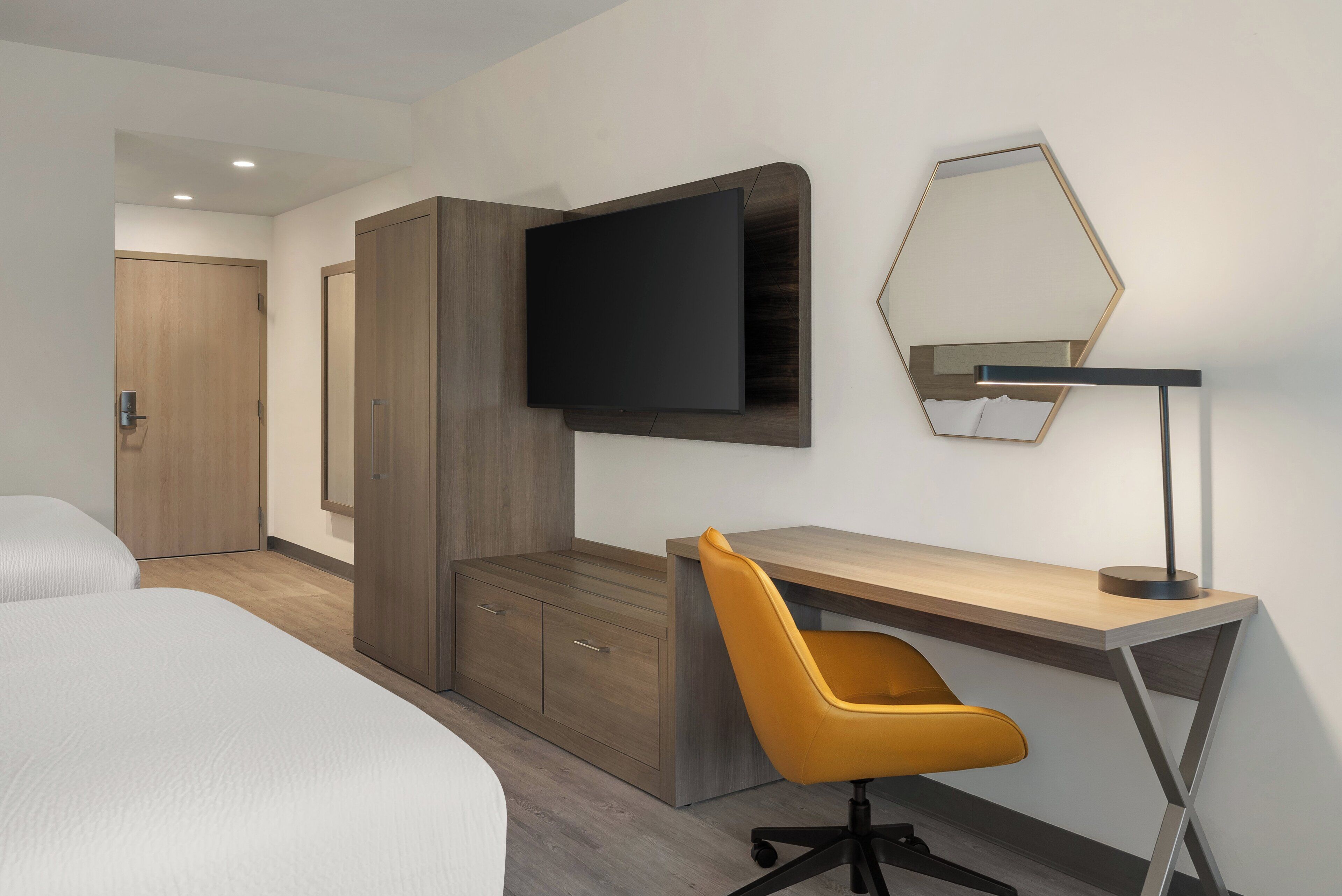 Een hotelkamer met een bed, een bureau met stoel, een flatscreen televisie en een spiegel aan de muur.