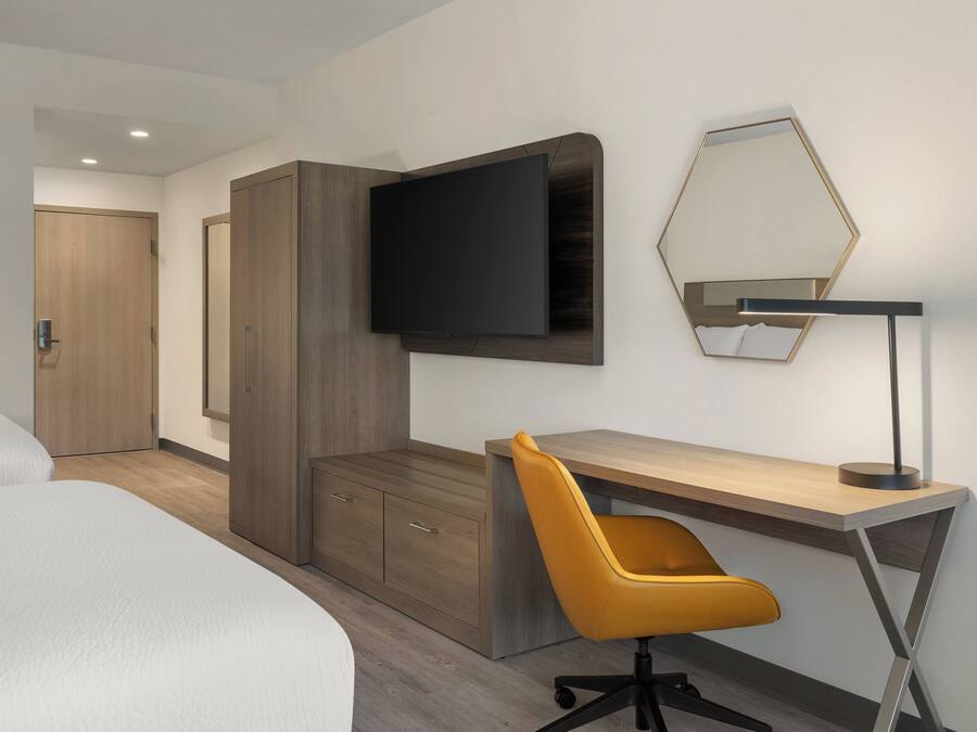 A hotel room with a bed, a desk with a chair, a flat-screen TV, and a mirror on the wall.