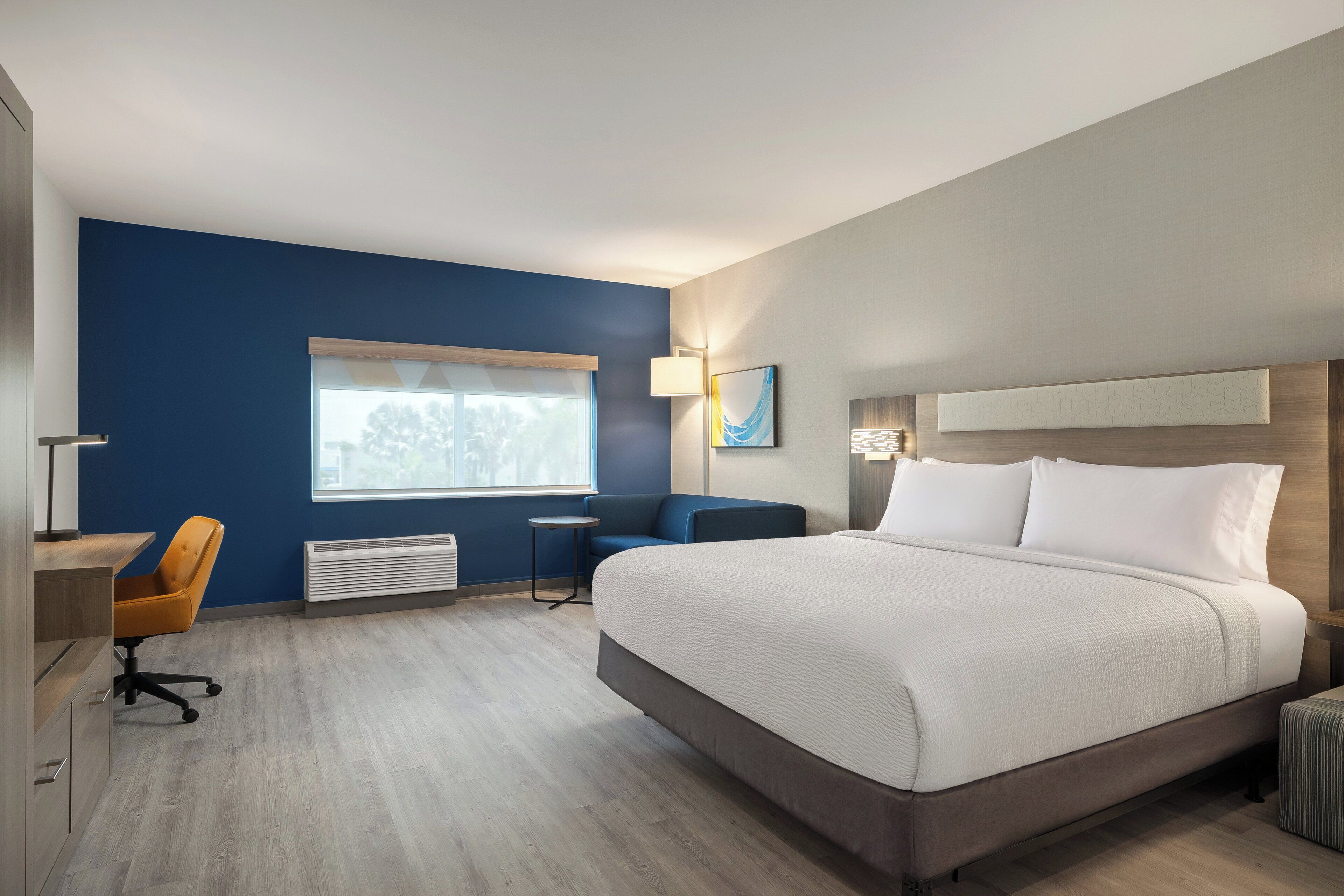 Une chambre d’hôtel équipée d’un lit, d’un bureau, d’une chaise, d’une fenêtre et d’une lampe fixée au mur.