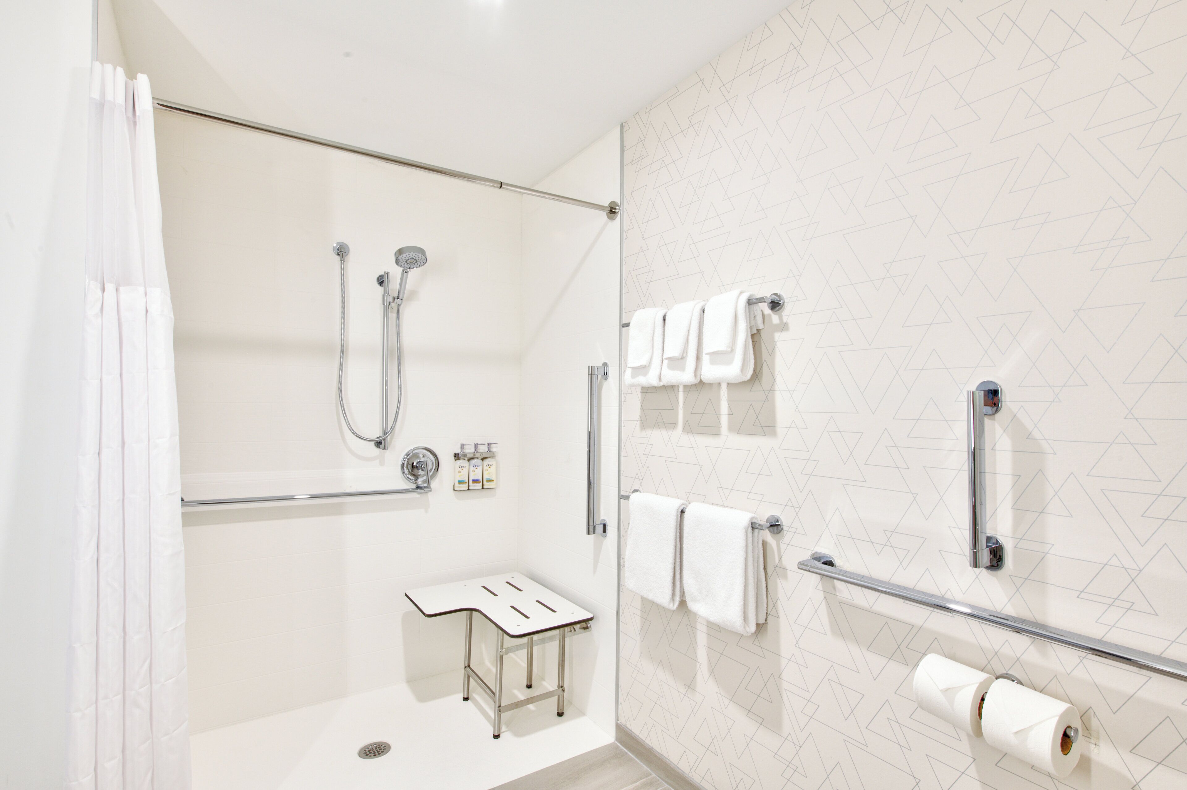 Un baño moderno con cabina de ducha de vidrio, un tocador pequeño con un taburete y un perchero con varias toallas.