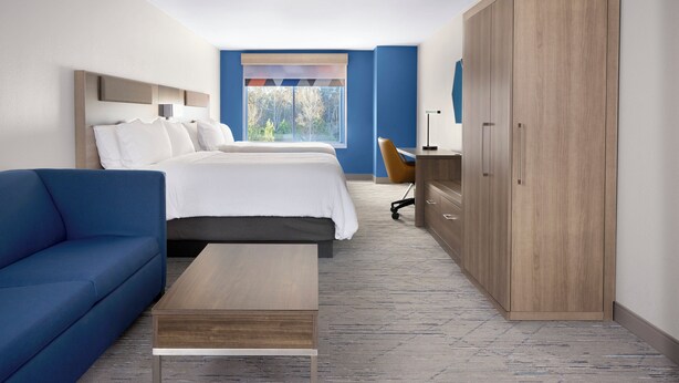 A hotel room with a bed, a blue sofa, a desk, and a wardrobe. - Holiday Inn Express & Suites Miami Intl Airport - 36th St (Miami)