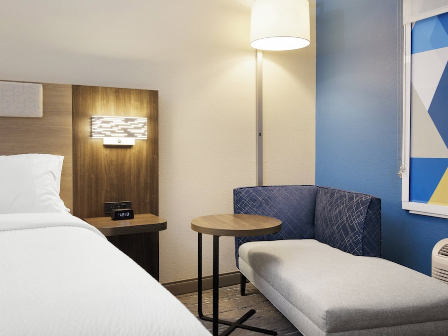 Habitación de hotel con cama, una mesita, una silla, una lámpara y una pared con diseño geométrico.