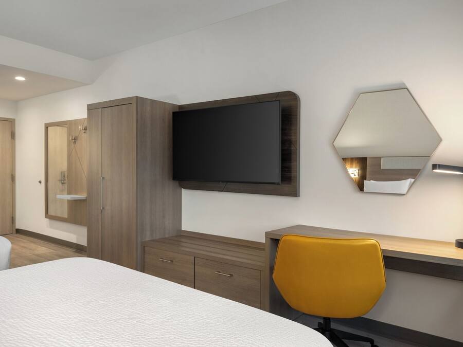 Habitación de hotel con cama, escritorio con silla, televisor, espejo y armario.
