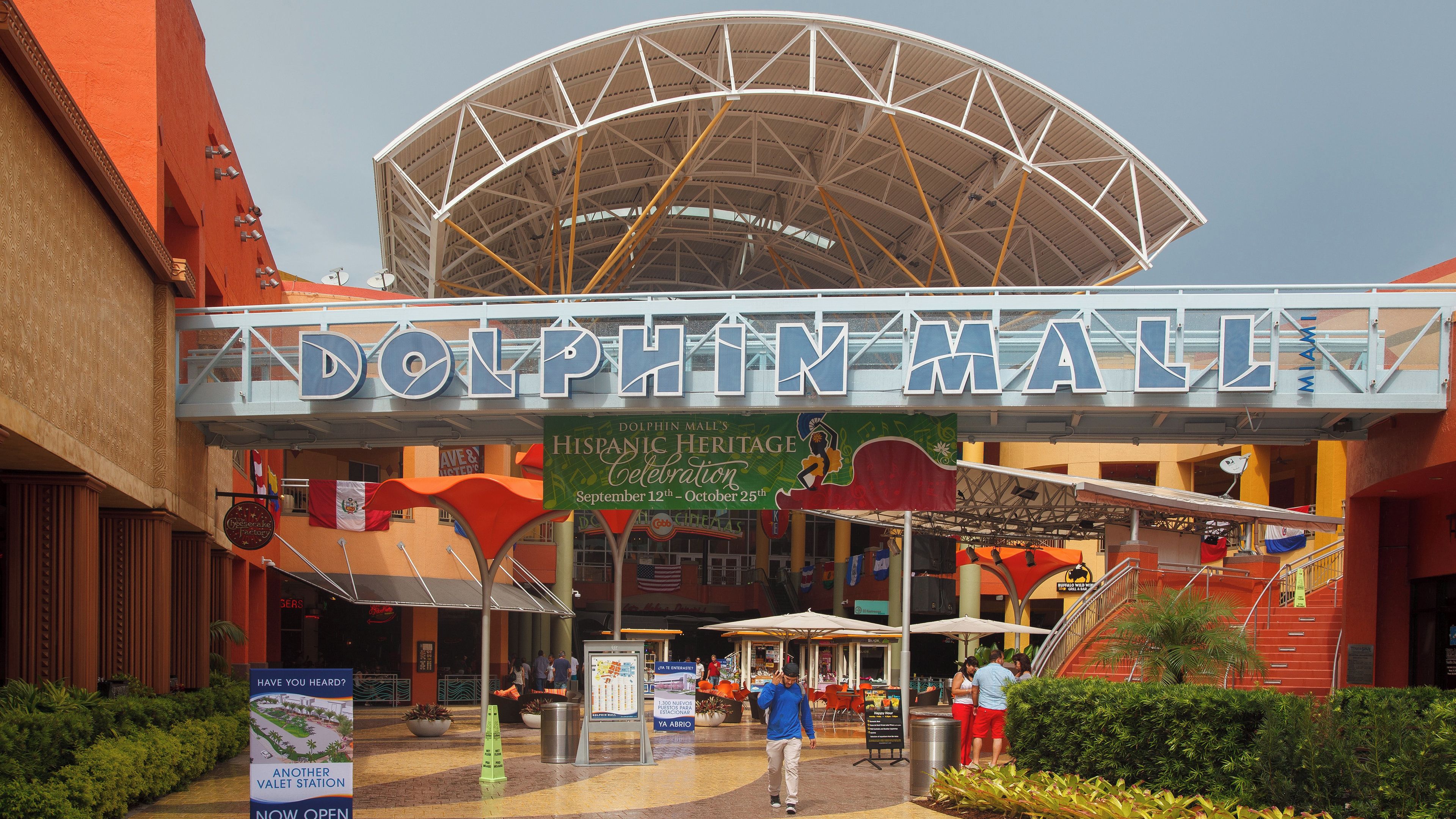 The Dolphin Mall entrance with a large sign, escalators, and a covered area with flags.