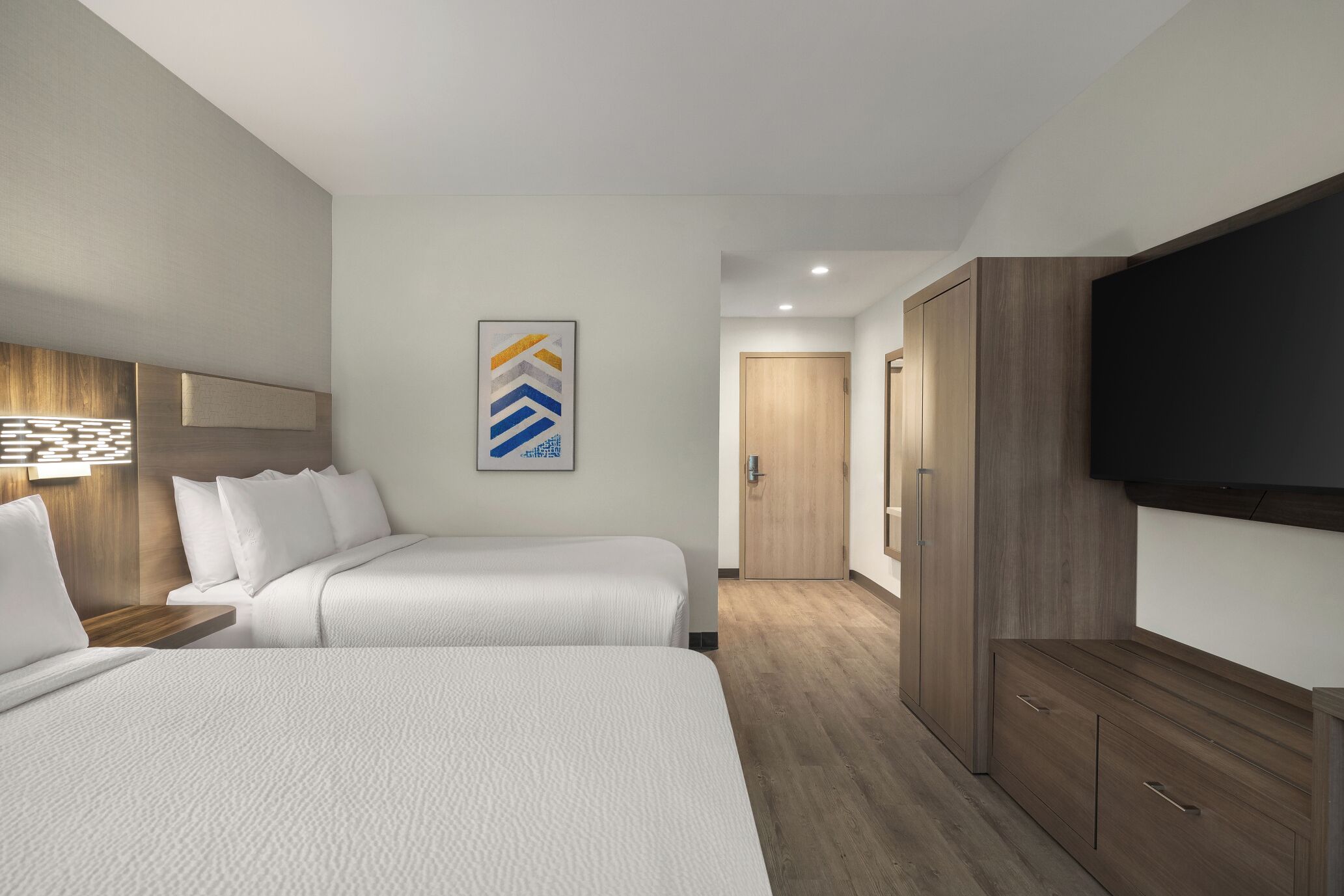 Habitación de hotel con dos camas, un televisor de pantalla plana, un armario de madera y una obra de arte abstracta enmarcada en la pared.