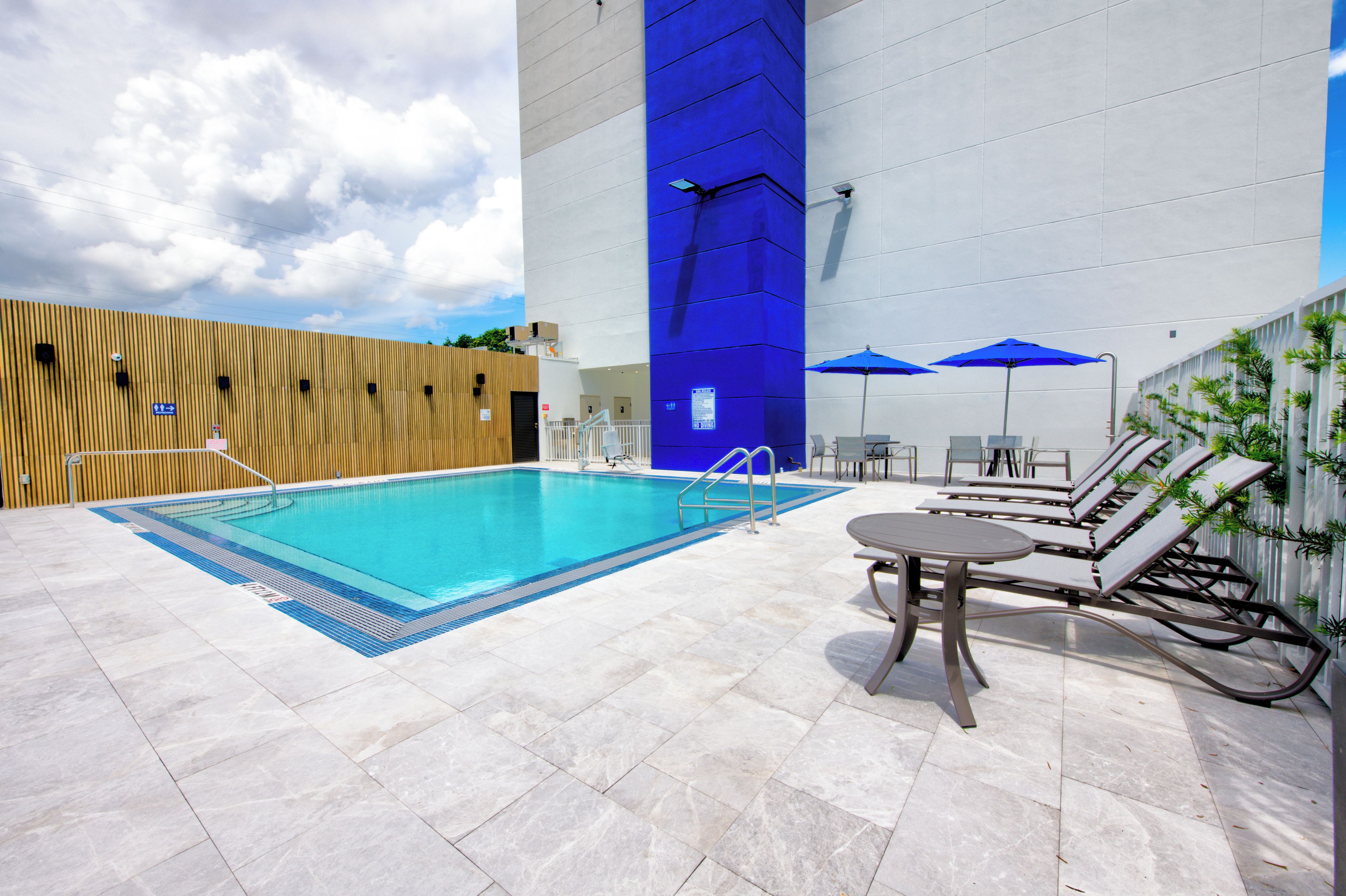 Una piscina con borde azul, sillas de descanso y sombrillas.
