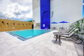 Ein Swimmingpool mit blauer Umrandung, Liegestühlen und Sonnenschirmen.