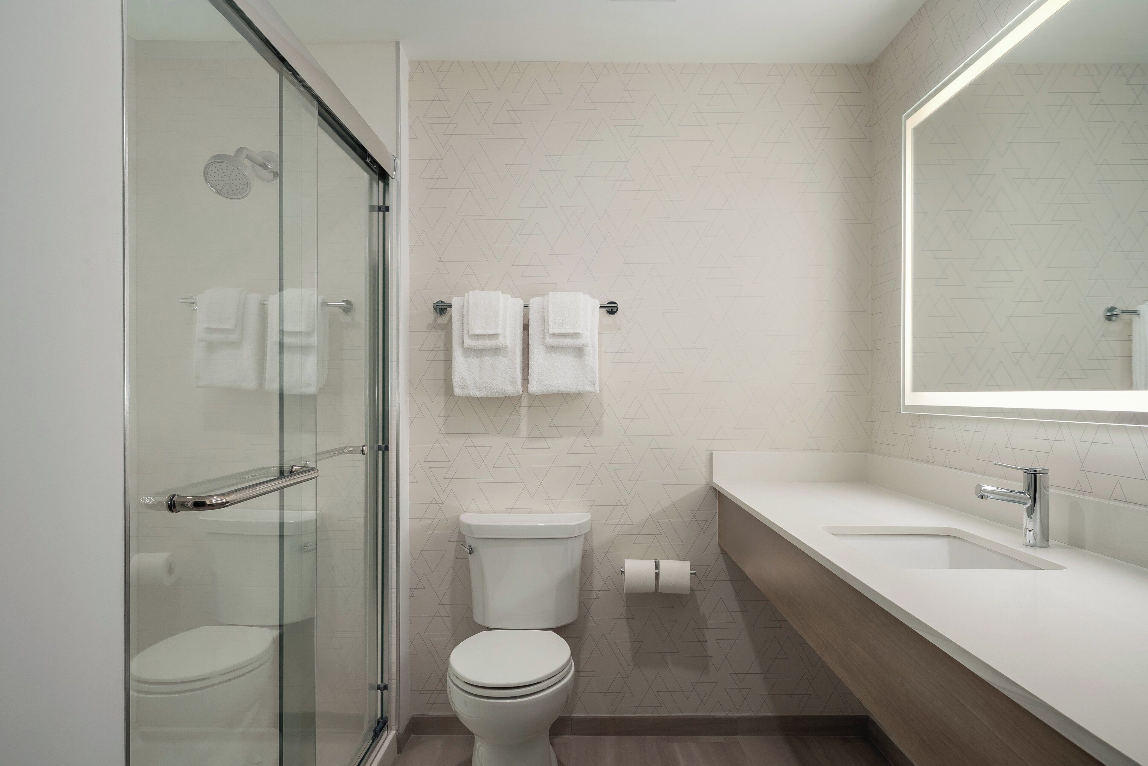 Une salle de bain moderne avec une douche à parois de verre, des toilettes et un lavabo surmonté d’un miroir.