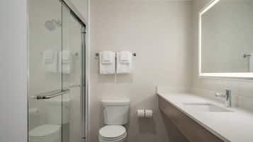 Une salle de bain moderne avec une douche à parois de verre, des toilettes et un lavabo surmonté d’un miroir.