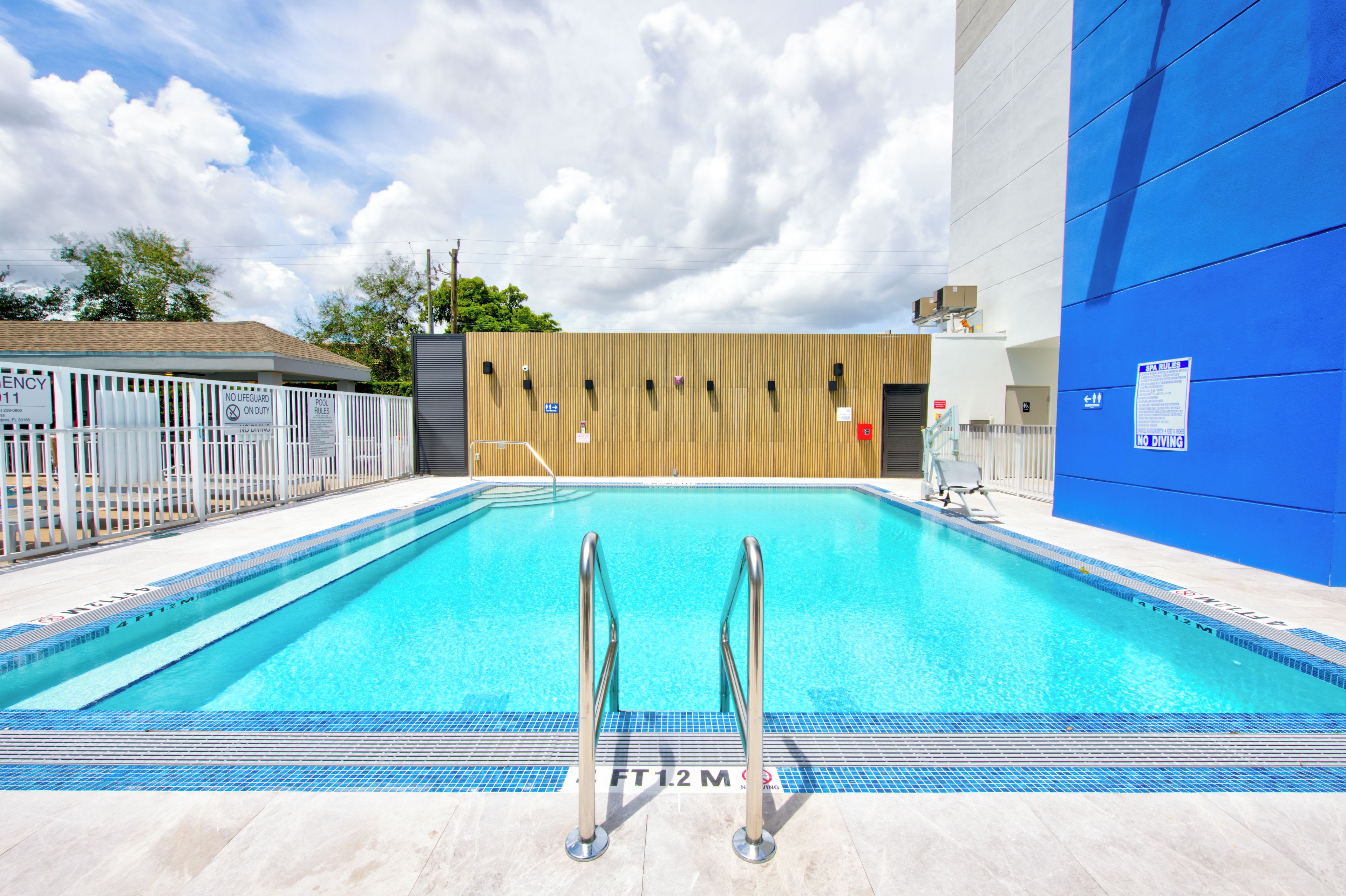 A swimming pool with a wooden wall and a blue building in the background.