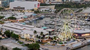 A waterfront area with a large Ferris wheel, marina, and various buildings including a hotel with a rooftop pool.